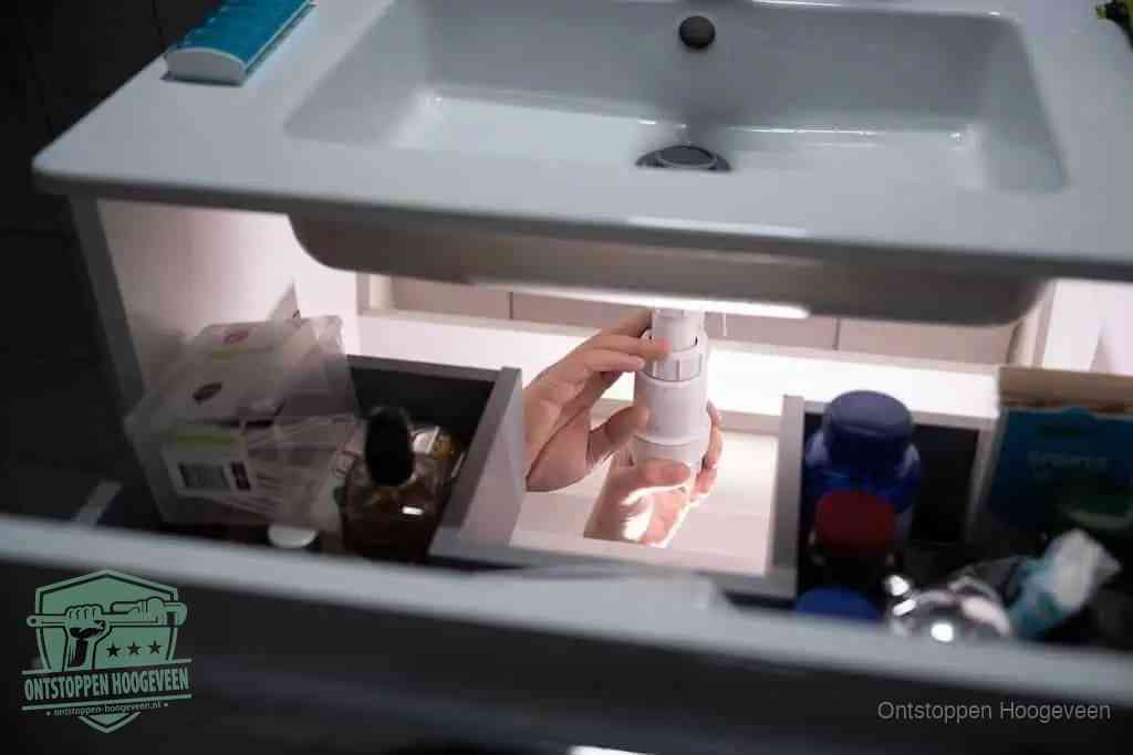 Een pompfles met zeep boven een wastafel, de heet water en afwasmiddel-methode om een vetprop in de afvoer los te maken in Hoogeveen