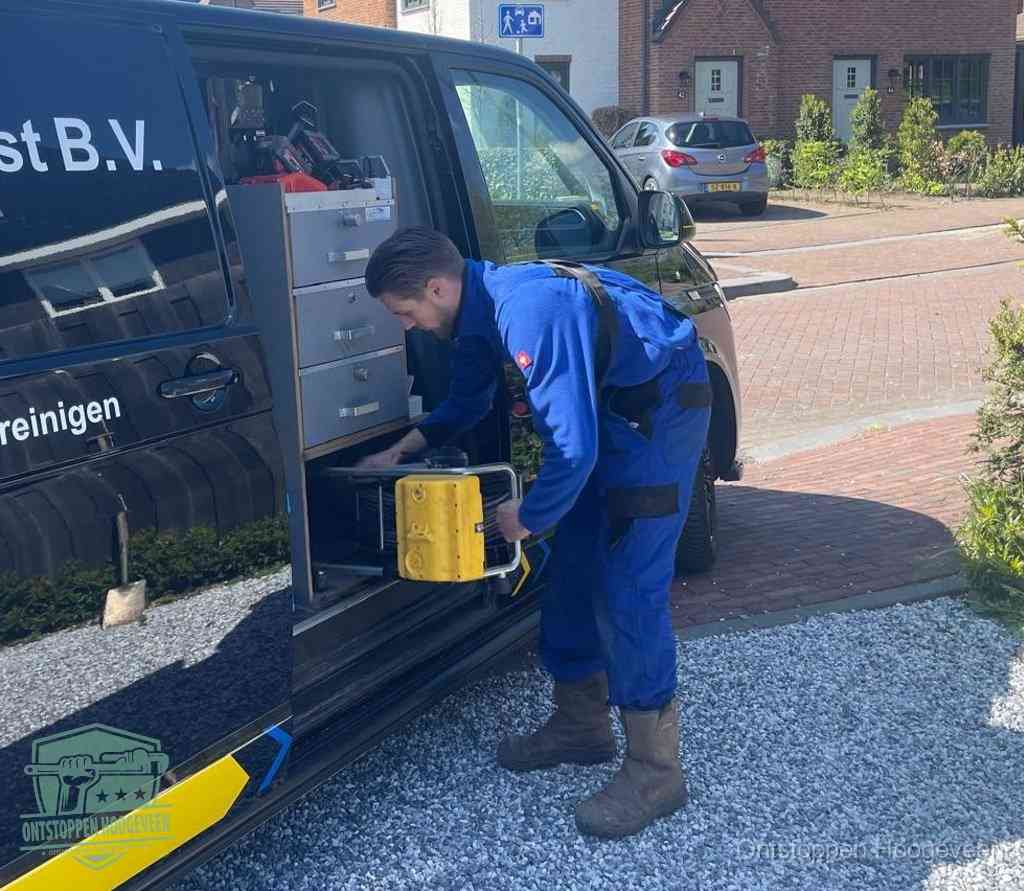 Een monteur pakt buiten op de oprit gereedschap uit de bedrijfsbus, het moment om een professional in te schakelen voor een verstopte afvoer in Hoogeveen