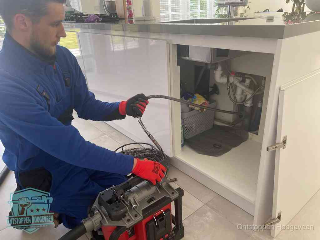 Monteur voert een ontstoppingsveer in de afvoer onder de keuken in Hoogeveen