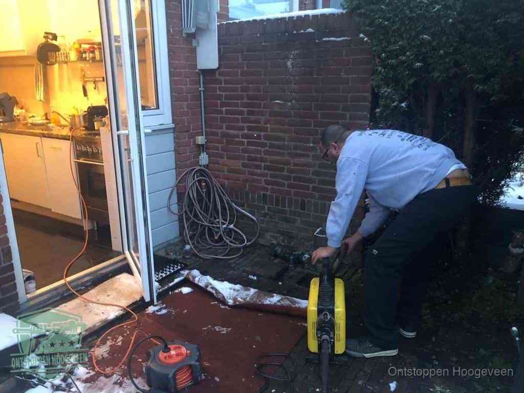 Een monteur werkt buiten bij een open riool-/grondput met een elektrische ontstoppingsmachine om een verborgen afvoerprobleem op te sporen in Hoogeveen