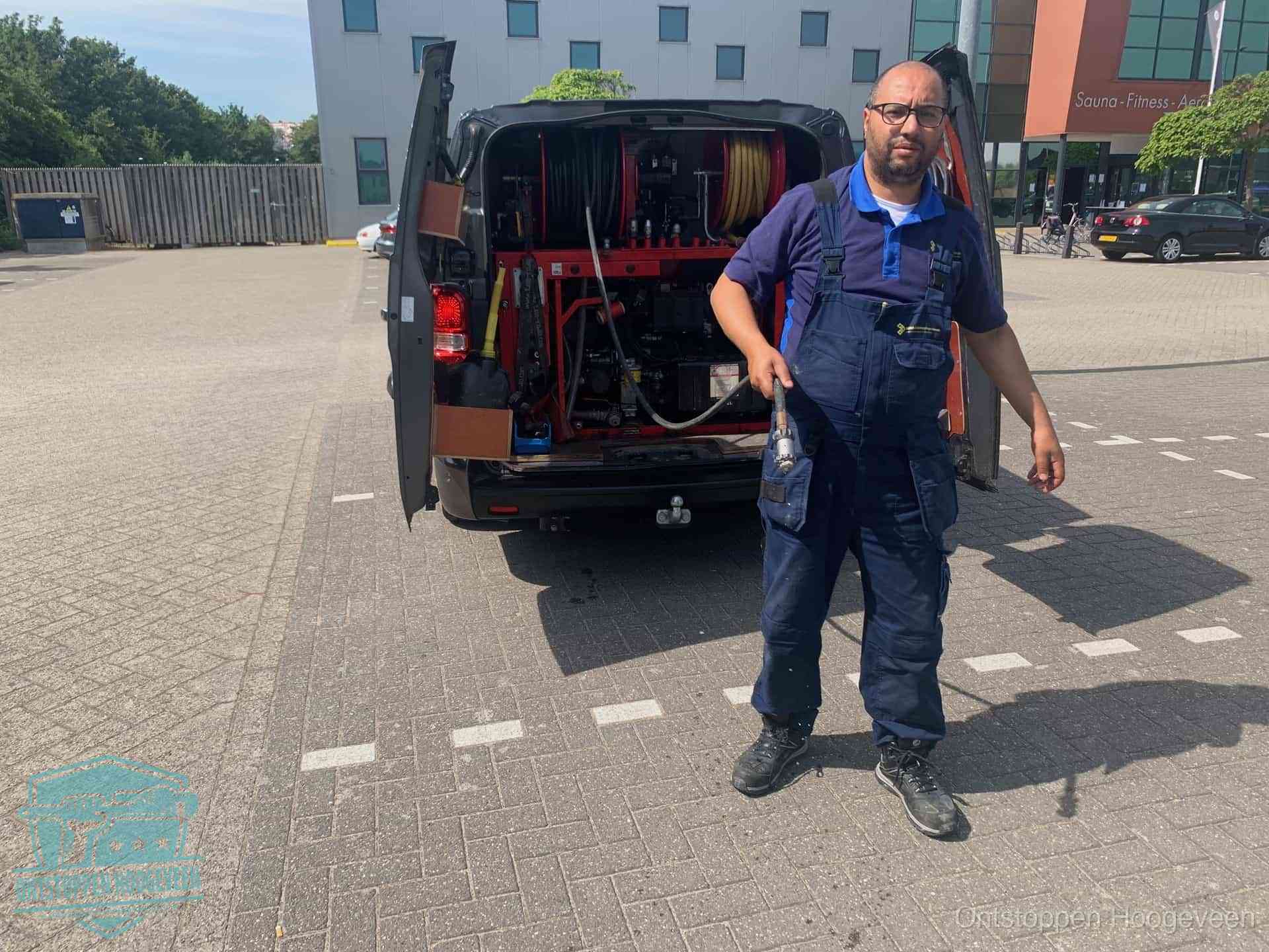 Een monteur bij zijn bestelbus met een hogedruk- en rioolreinigingsunit, klaar om de oorzaak van terugkerende wc-verstoppingen aan te pakken in Hoogeveen