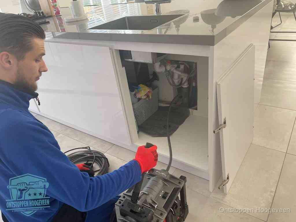 Monteur ontstopt met een veermachine een verstopte afvoer onder de gootsteen in Hoogeveen