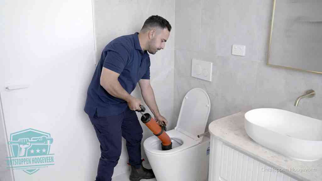Een monteur gebruikt een handmatige perspomp (toiletontstopper) op een wandcloset tijdens het professioneel wc ontstoppen in Hoogeveen